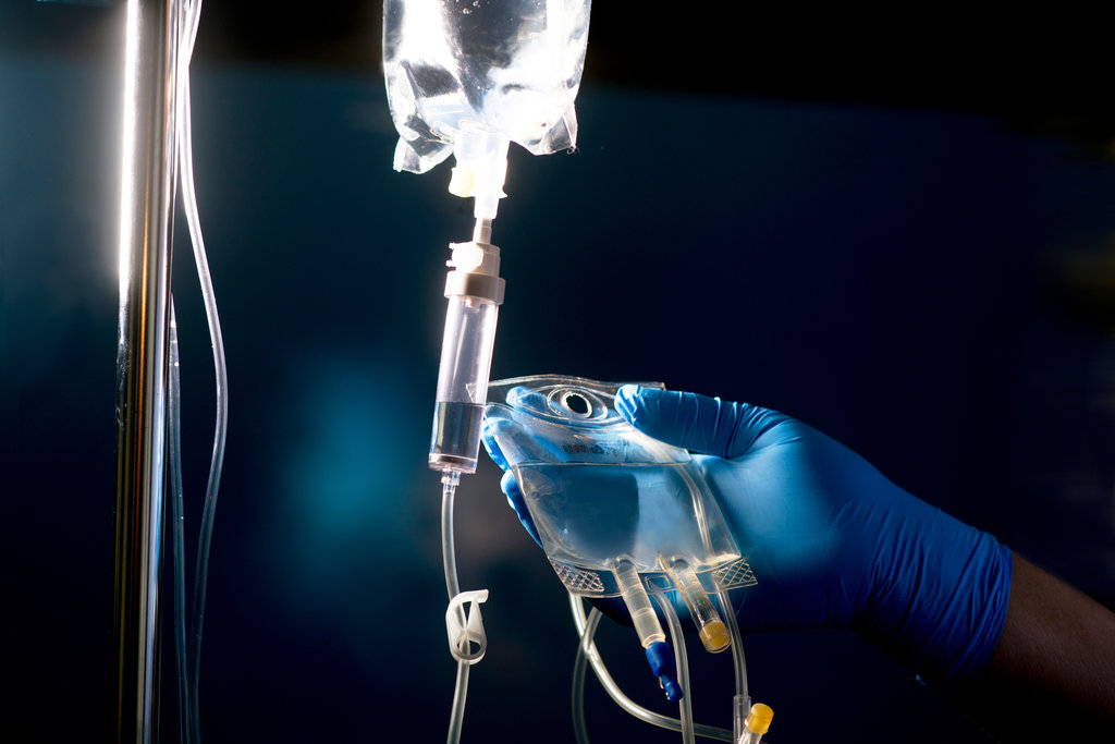 Nurse prepares secondary "piggyback" IV medication solution bag for administration with primary IV bag and IV tubing.