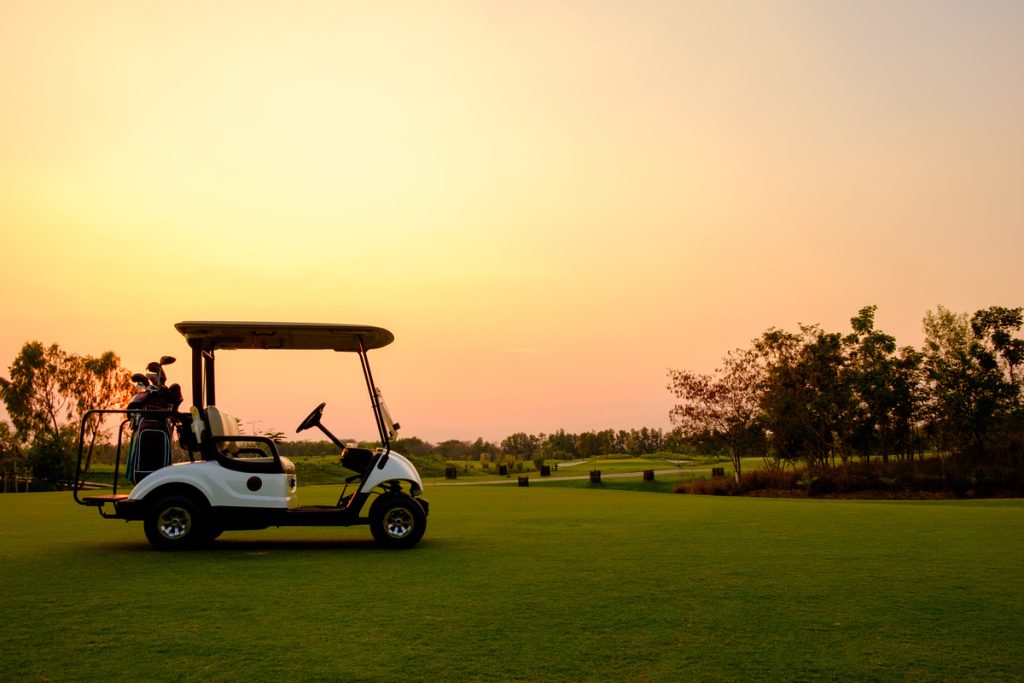 Golf cart car in fairway of golf course with fresh green grass field and cloud sky and tree on sunset time